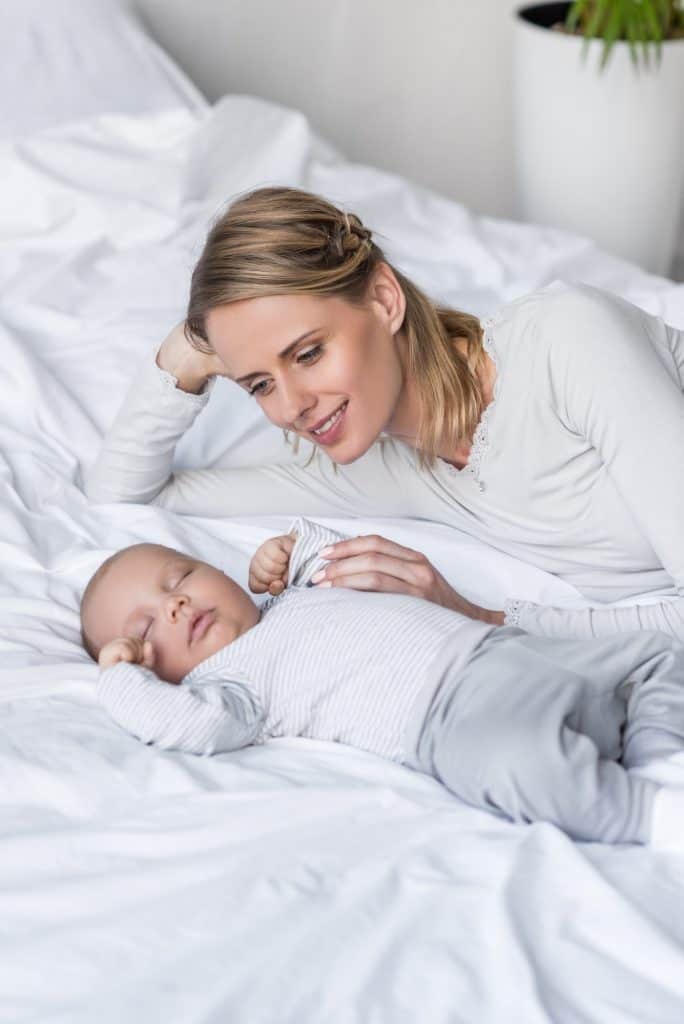 happy mother relaxing in bed with sleeping baby boy